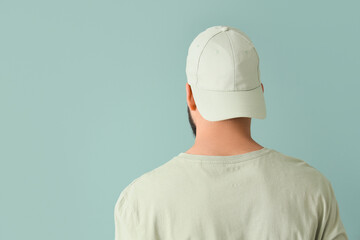 Handsome young man in stylish cap on blue background, back view
