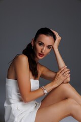 Elegant young woman in a white strapless dress and high heels posing in studio. Fashion model with...