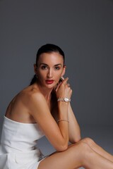 Elegant young woman in a white strapless dress and high heels posing in studio. Fashion model with...