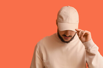 Naklejka premium Handsome young man in stylish cap on orange background