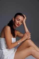 Elegant young woman in a white strapless dress and high heels posing in studio. Fashion model with...