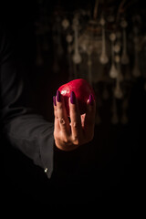 Image of a witch holding an apple in her hand, black background.