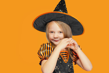cute little witch girl shows heart symbol with her hands, isolated on free orange background