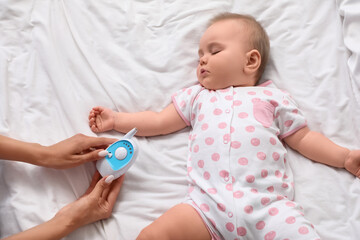 Female hands with radio nanny and cute sleeping little baby on bed at home