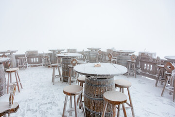 Snow-covered outdoor patio with barrel tables on a foggy winter day