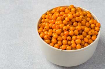 Bowl filled with sea buckthorn berries on a gray background, horizontal, close up. Concept of...