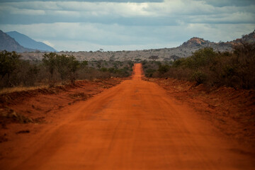 Red Dirt Road in African Savannah with Mountains in the Background