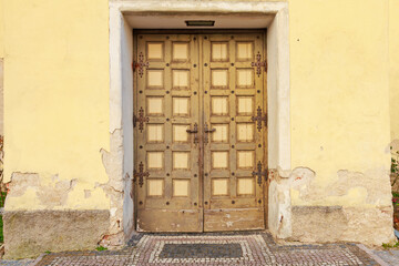 Rustic wooden door in worn yellow wall with stone mosaic pathway