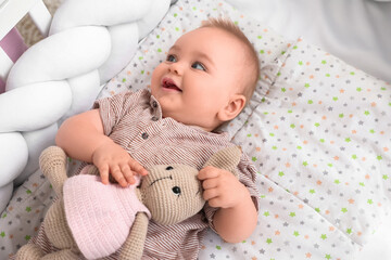 Cute little baby with toy lying in crib at home
