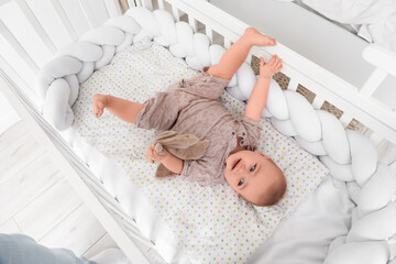 Cute little baby with toy lying in crib at home