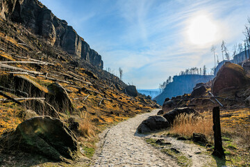Serene path through sunlit rocky landscape with dramatic cliffs and blue sky