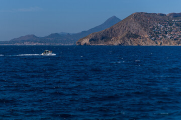 Naklejka premium Motor boat sailing on blue mediterranean sea, calm waves in the foreground, in the background Calpe & Altea