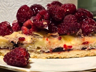 A delicious slice of raspberry tart or pie with a creamy filling and a flaky crust, topped with fresh, vibrant red raspberries.