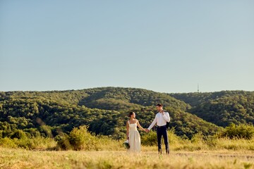 Bride and Groom Strolling Through Scenic Green Landscape in Summer