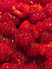 A close-up of vibrant red raspberries, with a glistening surface, showing their detailed texture...