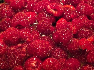 A close-up of a large pile of glistening, ripe raspberries in a  tart, with a rich, inviting red...