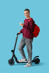 Male student with backpack and electric scooter using mobile phone on blue background