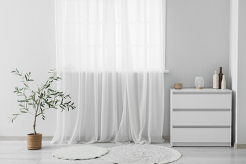 Interior of light room with curtain, commode and plant