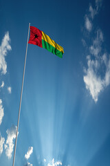Waving National flag of Guinea Bissau on flagpole in sky