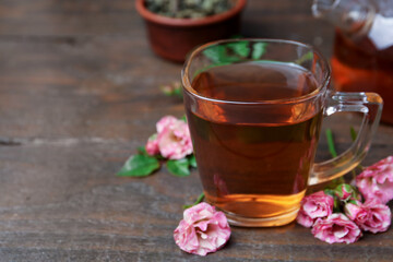 Tasty rose tea in glass cup and flowers on wooden table, closeup