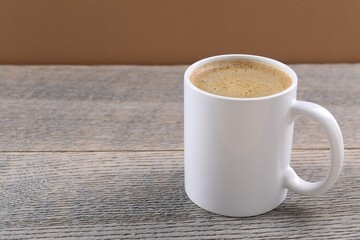 Aromatic coffee in cup on wooden table against brown background, closeup. Space for text