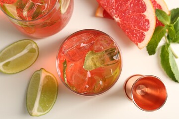 Tasty cocktail with ice cubes, lime and grapefruit on white table, flat lay