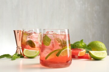 Tasty cocktail with ice cubes, lime and grapefruit on white table, closeup
