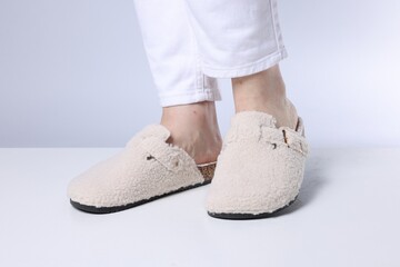 Woman in stylish white slippers on light floor against grey background, closeup