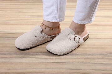 Woman in stylish white slippers on wooden floor, closeup