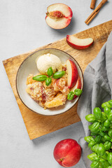 Peach crumble or cobbler with vanilla ice cream scoops and cinnamon in a plate on a wooden board