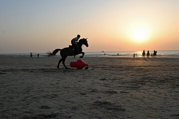 Pferd springt über eine rote Boje am Strand von De Haan Belgien bei Sonnenuntergang