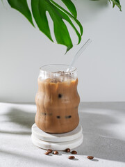 Ice latte coffee in a glass with milk and straw on a light background with coffee beans, monstera...