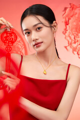 A young woman in a red dress holding a traditional ornament with a festive background Chinese word...