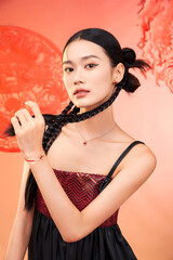 A young woman posing elegantly with braided hair and jewelry against a vibrant colored background.