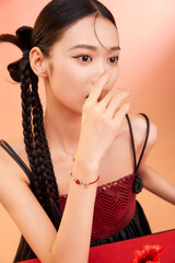 Young woman with braided hair poses thoughtfully wearing jewelry against a warm backdrop.