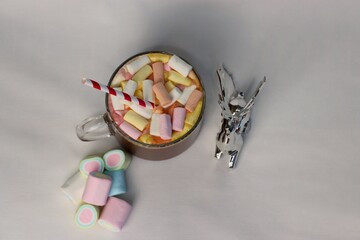 Top view of hot cocoa cup with colorful marshmallows and festive striped straw, next to decorative...
