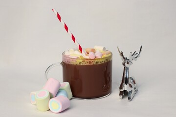 Hot cocoa cup with marshmallows and festive striped straw on white background — perfect cozy...