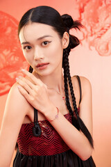 A young woman with braided hair showcasing jewelry against a red background Chinese word means...