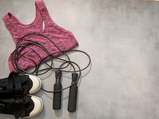 accessories for fitness and sports: skipping rope, weights, pink sports top. Top view.