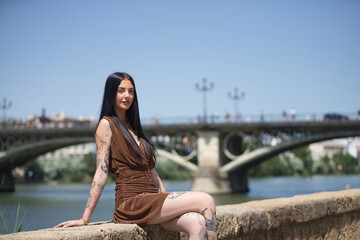 Young woman, brunette, tall, thin and very tattooed, with brown dress, posing looking at the camera...