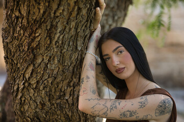 Portrait of a young woman, brunette, tall, slender and very tattooed, wearing a brown dress,...