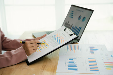 A professional businesswoman reviews financial documents using a calculator, pen, and laptop in the office, analyzing reports, charts, and graphs to manage budget, expenses, investment, and strategic 