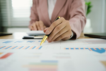 A professional businesswoman reviews financial documents using a calculator, pen, and laptop in the office, analyzing reports, charts, and graphs to manage budget, expenses, investment, and strategic 