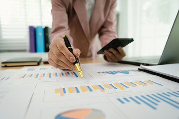 A businesswoman uses a calculator and pen while analyzing financial reports on a desk with charts and a laptop, symbolizing accounting, budgeting, finance, planning, and investment decisions.