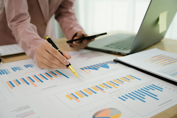 A businesswoman uses a calculator and pen while analyzing financial reports on a desk with charts and a laptop, symbolizing accounting, budgeting, finance, planning, and investment decisions.