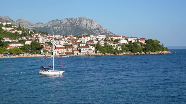 Scenic view of the coastal village on the Makarska Riviera, with a sailboat on the Adriatic Sea, mountains in the background, Croatia.Tranquil bay of a charming town with traditional houses at evening