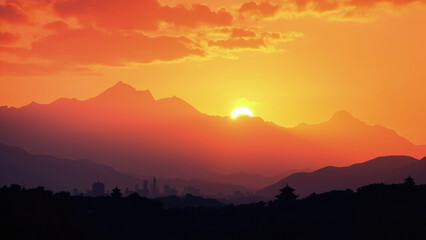 Sunset over mountain range with orange sky sun partially obscured by peaks silhouette of city buildings and trees