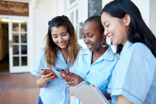 Three High School friends laughing whilst checking their mobile phones - Powered by Adobe