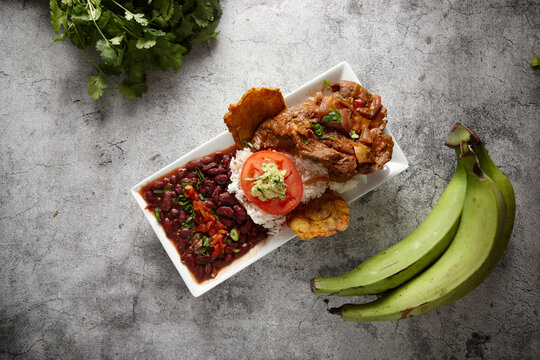 Beans rice and meat dish served in a rectangular plate on a concrete counter with green banana.