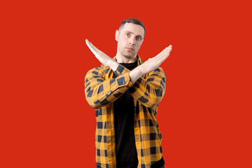 Young man crossing his arms in an X sign showing denial standing on isolated red background